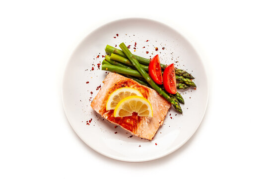 Garnished fried salmon steak with boiled green asparagus on white background. Top view