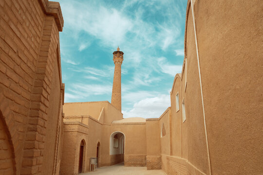 An alley in the old context of Semnan in Iran. A view of an old city with clay buildings and the brick minaret of a mosque.