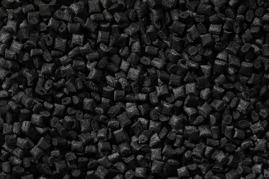 A top-down macro photo shows a dense, uniform layer of small, black, rectangular or cylindrical conductive polymer granules with a matte, textured surface.