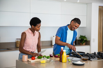 Diverse couple cooking on kitchen island, chopping lettuce and stirring sauce in frying pan