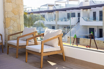 Naklejka premium Modern apartment balcony with wooden lounge chairs and glass railing overlooking urban playground