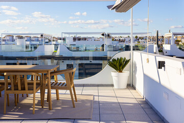 Naklejka premium Modern rooftop terrace with wooden dining set and glass railing in sunny residential complex