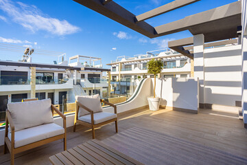Naklejka premium Modern apartment terrace with outdoor lounge seating and sunny view of residential complex