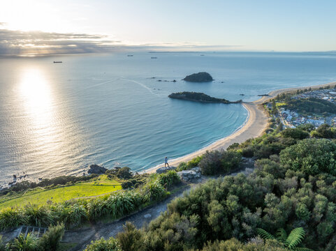 Aerial view of sun-kissed sands meet the turquoise sea, framed by the lush greenery of Mount Maunganui, a coastal paradise, Mount Maunganui, Bay of Plenty Region, New Zealand.