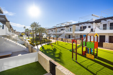 Modern apartment complex with green courtyard and children&rsquo;s playground in sunny tropical setting