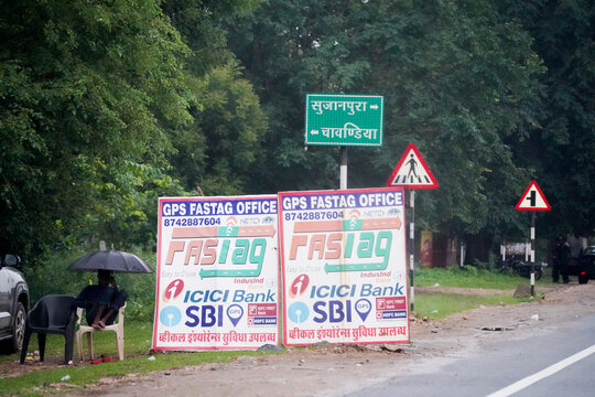 Roadside FASTag service office signs on an Indian highway, showing digital toll payment services, traffic infrastructure, and everyday travel environment.