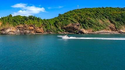 Naklejka premium Speedboat cruising through the vibrant turquoise waters of Koh Samed island, showcasing the rocky coastline and lush tropical greenery