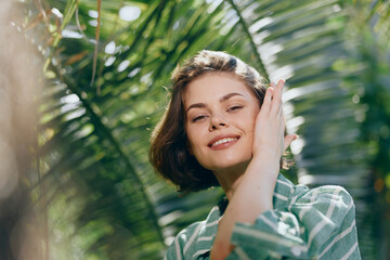 Fototapeta premium A cheerful woman relaxes outdoors amid lush greenery, smiling warmly as sunlight highlights her face.