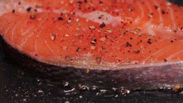 Close-up of appetizing juicy salmon steak sprinkled with black allspice frying in a pan.