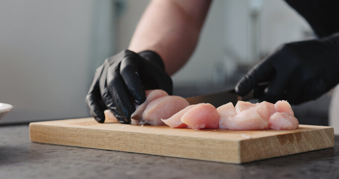 Man hands in black gloves cutting chicken fillet on oak board