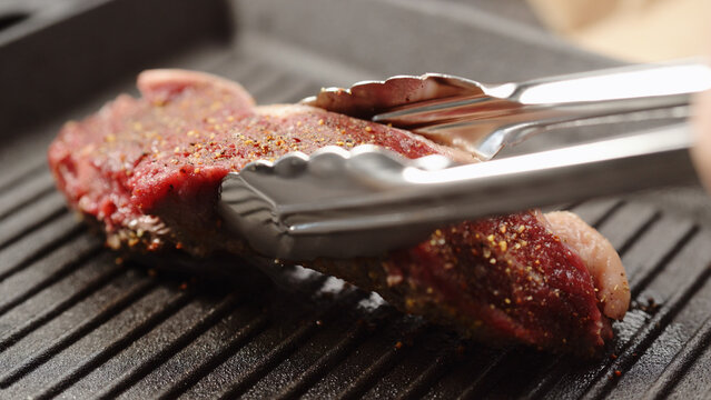flip new york steak with tongs on grill pan