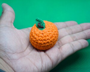 Handmade Amigurumi Orange Fruit Toy Held in Palm on Green Background