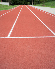 Red running track stretches into the distance with three marked lanes on a sunny day