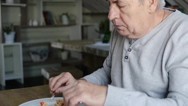 Happy senior man eating a scramble on a white plate with vegetables. Elderly male using knife and fork to cutting meal, has a breakfast. Balanced diet, cooking, culinary. Food concept. Old person