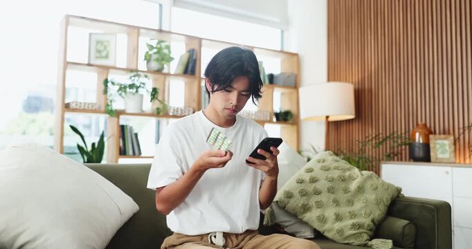 Home, pills and man on sofa, smartphone or reading label with prescription, internet or search for info. Health benefits, warning or Asian person on couch, cellphone or app for medicine or supplement