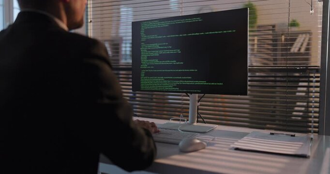Programmer developer coder in office computer coding. Businessman engineer man reviews code on monitor, seated at desk in corporate workspace. Clear concept of modern office coding at work.