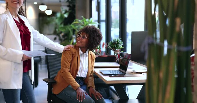 Caring manager providing support and positive encouragement to her african american female employee, tapping her shoulder in a gesture of empathy and solidarity at the office workspace