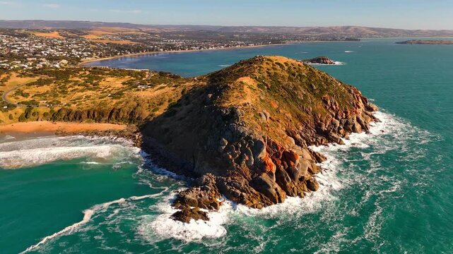 Aerial establishing medium of coastal cliffs and turquoise waters at Victor Harbour Bluff with golden sunset light, orbit with homes in backdrop