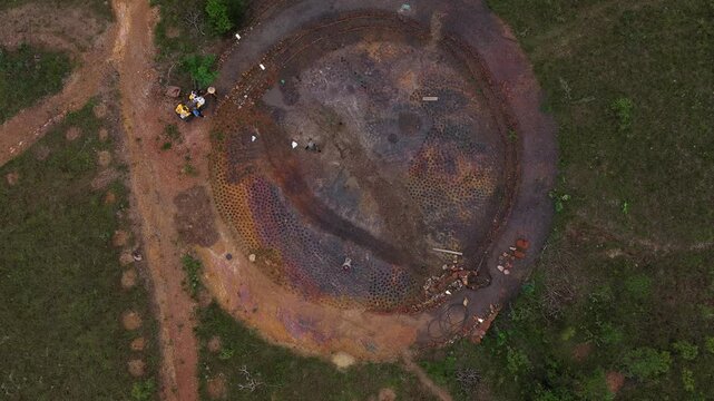 Drone ascending and spinning view of a circular soil regeneration site in the Cerrado Goiano, showing patterned planting pits, erosion control layout, and workers positioned around restoration area