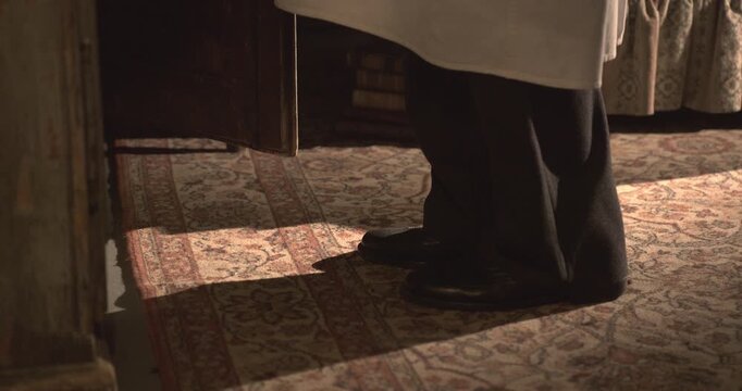 Men's black vintage shoes walk over an old carpet toward a wooden box, camera pan, 1950s style.