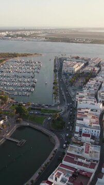 Vertical aerial orbit capturing Ayamonte city and marina landscape with Portugal visible across the Guadiana River in the background.