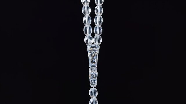 Close-up of a clear, translucent prayer bead string with a decorative separator against a dark background.