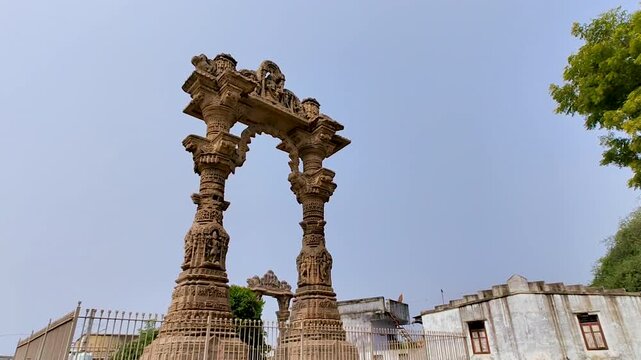 Vadnagar Gujarat India Narsinh Maheta Ni Chowri historic stone pillars with Kirti Toran background, ancient Hindu monument, cultural heritage architecture under clear sky.