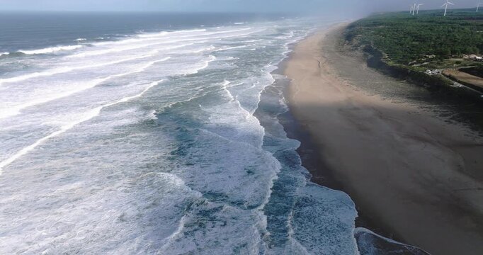 Drone aerial along Nazare Portugal beach, long shoreline with Atlantic waves breaking in parallel lines, cinematic coastal seascape with sand and surf