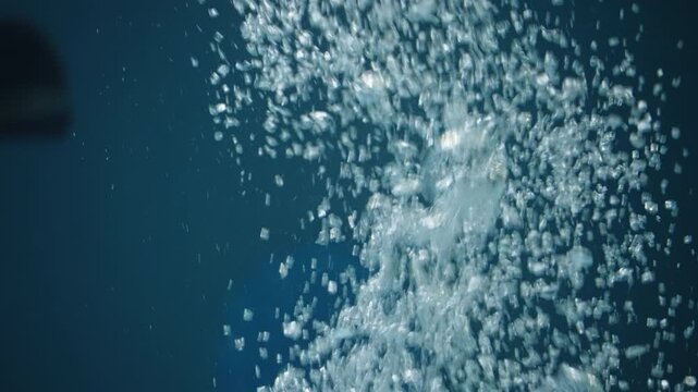 Close-up underwater view of sparkling air bubbles rising through deep blue water, capturing effervescent motion, fluid turbulence, and shimmering textures in an aquatic scene