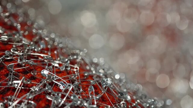 Macro close-up of intertwined silver safety pins clustered on red textured fabric with bokeh highlights and shallow depth of field creating an abstract craft composition