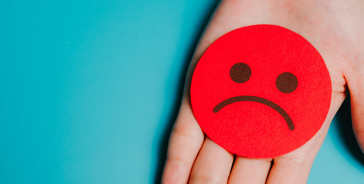 Feedback concept. Red sad face icon on hand showing negative emotion and disappointment with blue background