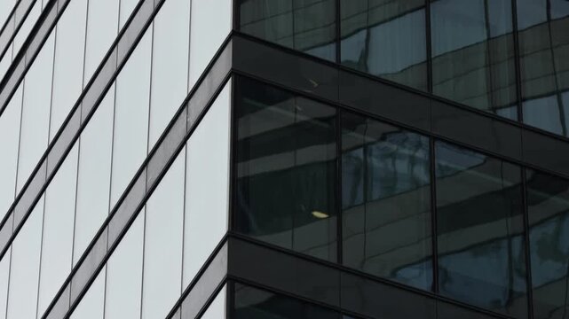 Close-up of a modern glass-clad office building facade with reflective windows, sharp geometric lines, and angular corner details highlighting contemporary architecture.