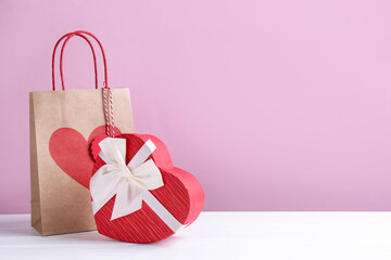 Paper bag and heart shaped gift box on white table against pink background, space for text....