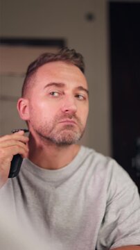 Vertical video Man preparing for presentation, Caucasian male getting ready by trimming facial hair in contemporary bathroom before important presentation, Modern bathroom setting with man shaving
