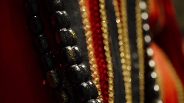 Dramatic macro close-up of layered beaded necklaces with glossy black beads, shimmering gold chains, and vibrant red strands, shot with shallow depth of field and warm bokeh