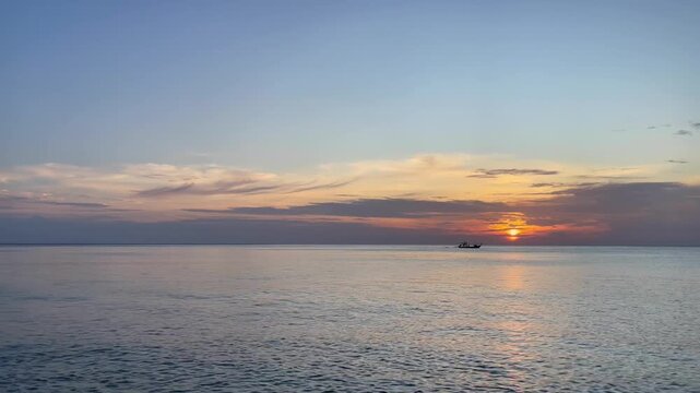 Peaceful sunset over a calm sea with a small fishing boat silhouetted on the horizon. Soft evening light and tranquil water create a relaxing seascape ideal for travel, tourism, and wellness concepts