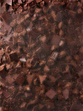 Assorted chocolate pieces are visible through wet glass covered with water droplets. The arrangement shows broken bars, shards, and pearls with rich layers and deep hues that indicate indulgence