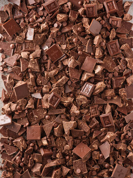 Different types of dark chocolate bits are laid out on a surface. They include chunks, chips, and small squares. This setup is for making treats and desserts in a kitchen
