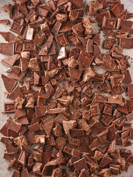 Small pieces of chocolate are scattered across a flat surface in a kitchen. The light from outside shows that it is daytime. These pieces are ready for use in a dessert