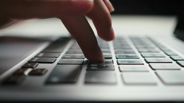 Extreme close-up, low angle video of agile fingers rapidly typing on a metallic silver laptop. Razor-sharp focus on swift movements during intense digital work. Focused aesthetic.
