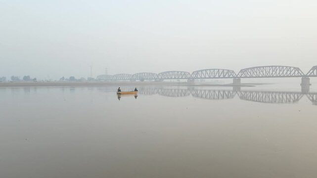 Fishermen in a boat, sailing on the water of a river, with a huge bridge in the background. Drone Video, 4K, Aerial Panning Shot.