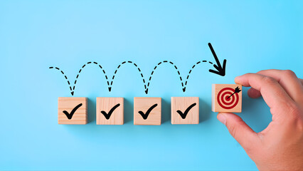 Hand placing a target block after a series of completed checkmark steps, symbolizing strategic goal achievement, successful progression, and business milestone completion
