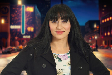 A woman with long black hair and a purple jacket is smiling for the camera