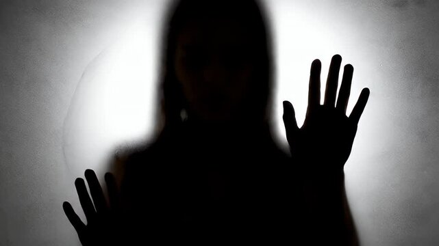Silhouette of a Person with Hands Pressed Against a Frosted Glass in Front of a White Light Source Creating a Dramatic