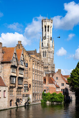 Fototapeta premium Medieval Belfry of Bruges tower and historic brick houses along the canal in Bruges, Belgium on a sunny day