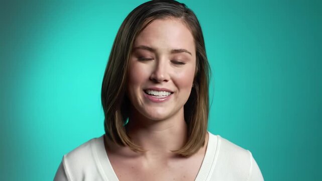 Young caucasian woman, white v-neck top, transitions expressions in a teal studio video, soft-lit, shallow depth of field. Concept of varied human emotions