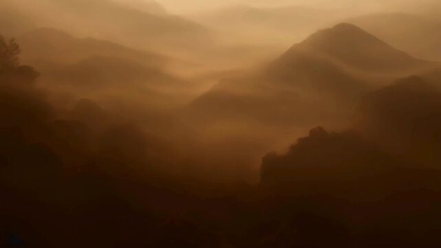 Atmospheric layers of mountain silhouettes covered in thick rolling mist and fog in a monochrome sepia or brown tone.