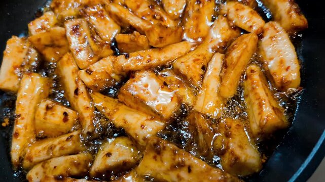 Sliced yellow plantain marinated with paprika and chilli spices fried on black cast iron pan, making patacones or kelewele