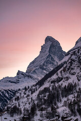 Matterhorn mountain landscape in Switzerland with snow covered peaks and a soft pink sky during winter sunset near Zermatt.
