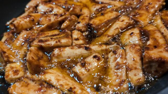Sliced yellow plantain marinated with paprika and chilli spices fried on black cast iron pan, making patacones or kelewele